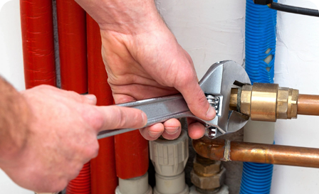 A person holding a wrench over the water pipe.