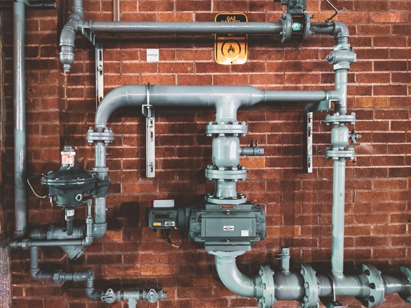 A red brick wall with pipes and valves on it.