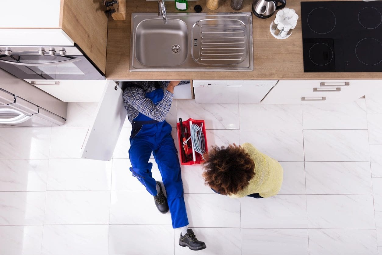 A person sitting on the floor in front of a sink.